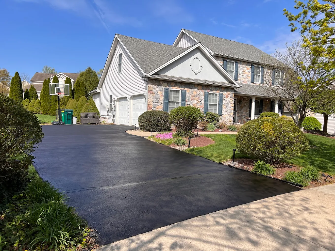 Sealcoated driveway with basketball hoop next to stone-and-siding home