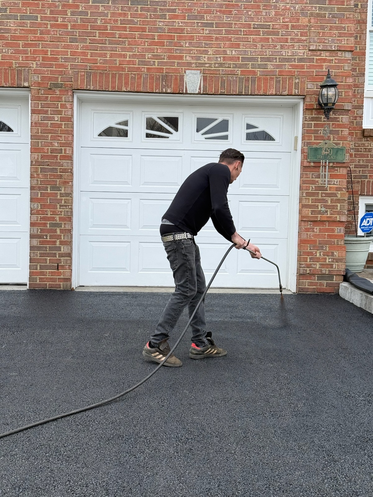 Crew member hand-spraying oil-based sealcoating on brick-home driveway