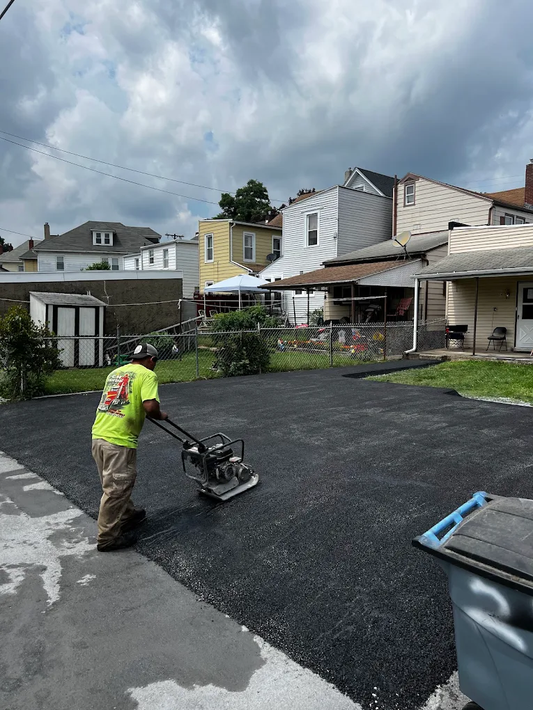 Crew member compacting new asphalt driveway with plate compactor
