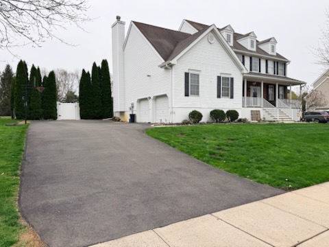 Worn asphalt driveway at white colonial home before sealcoating