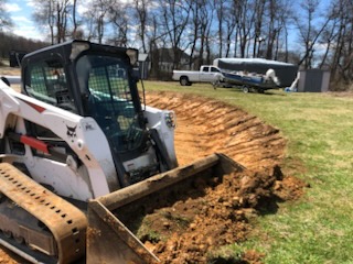 Skid steer grading a curved driveway pad in a rural yard