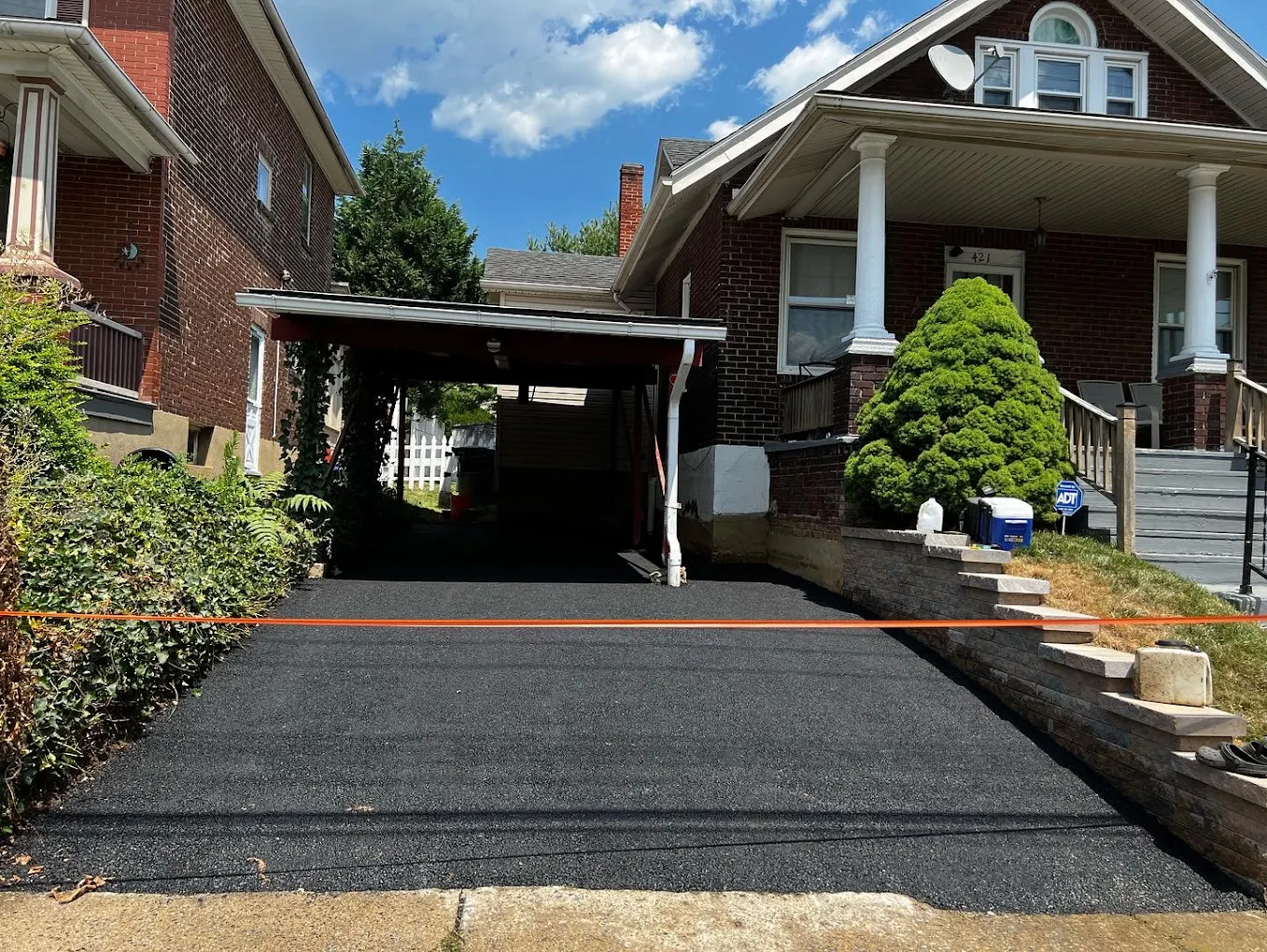 Sealcoated driveway between two brick homes under carport