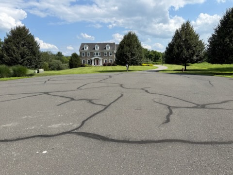 Wide asphalt driveway with spiderweb cracks needing crack filling and sealcoating