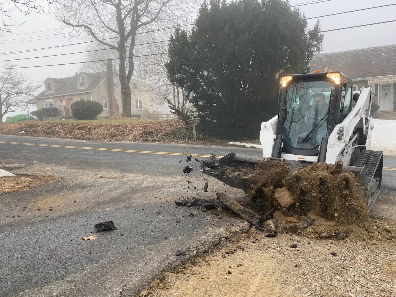 Bobcat skid steer removing damaged asphalt from roadway